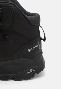 Black hiking boot featuring a textured fabric upper, Gore-Tex branding, rubber outsole with pronounced grip patterns, and a padded collar.