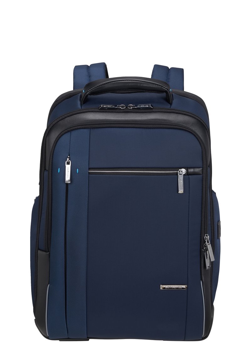 Zaino blu navy con dettagli neri, tessuto testurizzato, spallacci regolabili doppi, maniglia superiore e molteplici scomparti con zip.