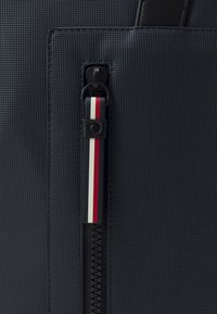 Borsa a spalla testurizzata blu navy con zip e tirante in pelle, e un accento a righe rosso, bianco e blu.