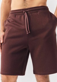 Shorts en coton mélangé marron avec une taille élastique, un cordon de serrage réglable et des poches latérales, présentant une texture douce et un design ajusté.