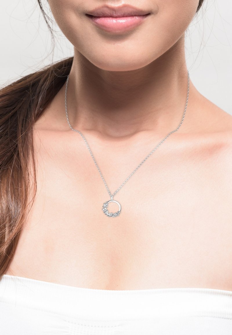 Sølv halskæde med en cirkulær vedhæng med bladaffekter. Kæden er tynd, og vedhænget ligger lige over kravebenet.