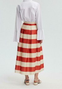 Jupe rayée rouge et crème en tissu lisse, avec un design plissé, taille haute, et longueur cheville. Associée à un chemisier blanc.