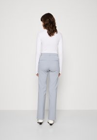 Jasnoszare spodnie o prostym kroju, wykonane z gładkiego materiału, z kieszeniami z tyłu i średnim stanem. Noszone z białą bluzką.