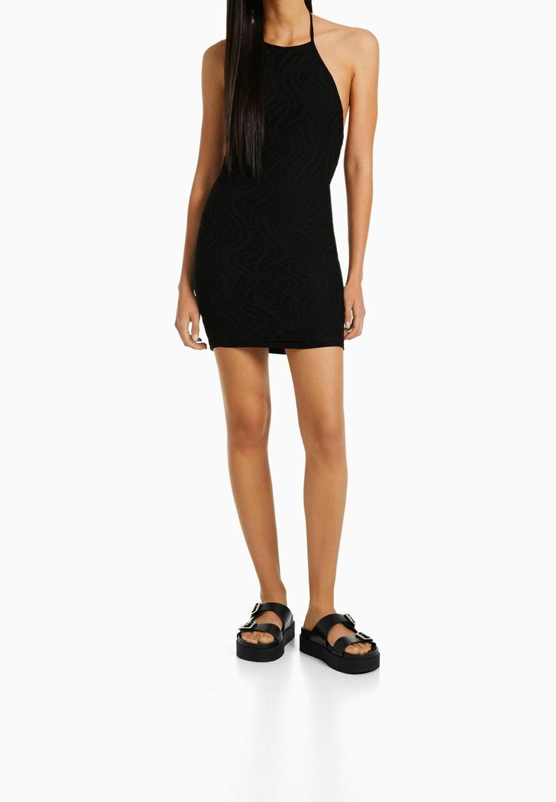 Robe courte noire à encolure halter avec un motif ondulé texturé, assortie à des sandales plateformes noires épaisses avec un détail de boucle métallique.