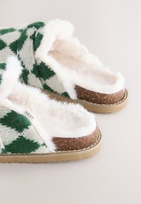 Chaussons en tricot verts et blancs avec une doublure douce et pelucheuse, une semelle ressemblant à du liège, et un motif à losanges.