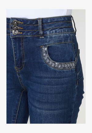 Vaqueros de mezclilla con un lavado azul oscuro, que cuentan con tres botones metálicos en la cintura y un bolsillo adornado con lentejuelas plateadas.
