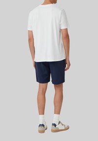 T-shirt en coton blanc à manches courtes, associé à un short marine foncé. Les chaussures sont blanches avec des accents bleus et beiges. Design décontracté.