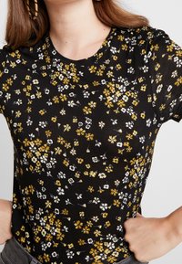 Camisa negra de manga corta con un estampado floral que presenta flores amarillas, blancas y grises. Tejido suave con escote redondo.