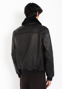 Veste bomber en cuir noir avec un col en fourrure douce noire et des poignets côtelés. Texture lisse et design ajusté. Vue de dos.