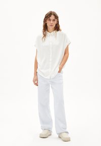 White short-sleeve button-up shirt, paired with light blue wide-leg pants and beige slip-on shoes. Smooth fabric, relaxed fit, minimal design.