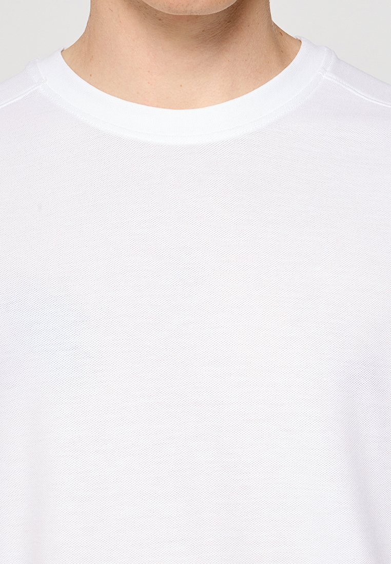 Nahaufnahme einer Person, die ein schlichtes weißes T-Shirt mit Rundhalsausschnitt trägt, das Nacken und oberen Brustbereich zeigt, vor einem einfarbigen Hintergrund.