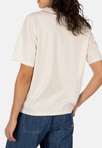 Short-sleeve, cream-colored T-shirt made of soft material, featuring a relaxed fit and simple design with no visible embellishments.