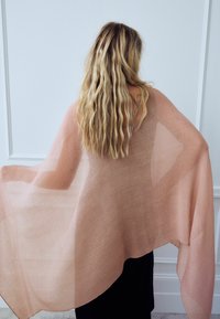 Châle rose transparent avec une texture côtelée, tombant élégamment des épaules. Tissu léger et doux avec un subtil éclat, améliorant l'attrait visuel.