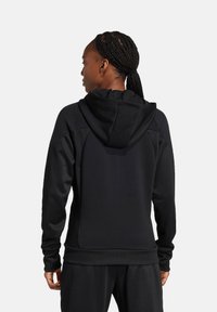 Felpa con cappuccio nera realizzata in tessuto testurizzato; presenta un design aderente, maniche lunghe e un discreto dettaglio di cucitura sul retro.