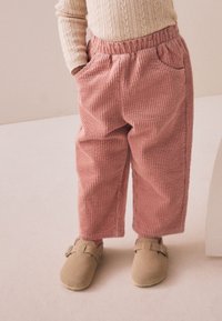 Pehmed roosad kordsitud püksid vertikaalsete soontega, millel on elastne vöökoht ja küljetaskud, kantud koos pruunide libisemiskindlate kingadega.