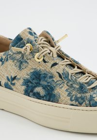 Nærbillede af beige vævet sneaker med blåt blomstermønster, beige elastiske snørebånd, gyldne øjebolte og tyk cremefarvet gummisål.