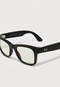 Lunettes de soleil Ray-Ban noires avec des montures rectangulaires, des verres teintés en vert et une petite icône de caméra à l'avant. Logo sur le côté.