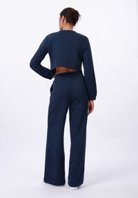 Sweatshirt court en coton bleu marine et pantalon large avec une taille élastique. Comprend des manches longues et un détail découpé à l'arrière.