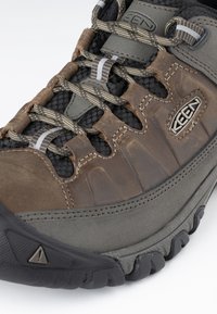 Gros plan sur une chaussure de randonnée marron et grise avec une semelle texturée, des lacets à motifs et un logo "KEEN" sur le panneau latéral.