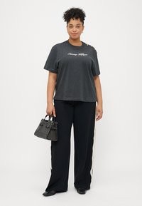 Szara bawełniana koszulka z logo "Tommy Hilfiger", krótkie rękawy oraz ozdobne guziki na ramieniu, zestawiona z czarnymi spodniami o szerokich nogawkach i małą czarną torebką.