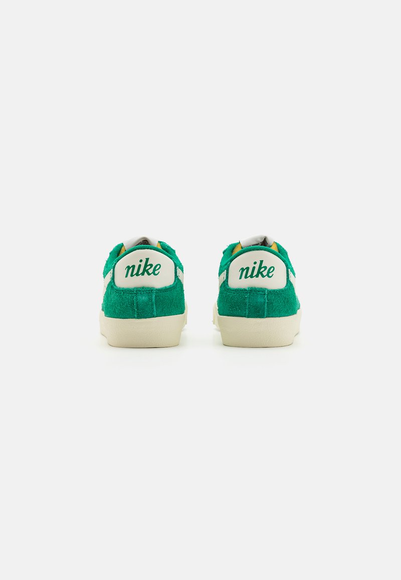 Zapatillas de ante verdes con detalles blancos y el logo "nike" en el talón. La lengüeta tiene un detalle amarillo. Diseño de perfil bajo.