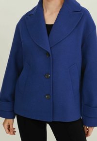 Blå jacka i ullblandning med bred krage, framknäppning med knappar, två sidofickor och avslappnade ärmar.