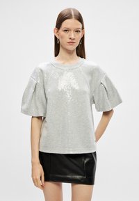 Hall vaipadega hall särk, millel on ees sädelevad detailid, lühikesed puhvärkiga varrukad ja ümmargune kaelus. Kombineeritud musta nahkmini seelikuga.