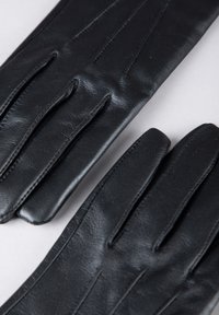 Black leather gloves with a smooth texture, featuring multiple stitched seams and five finger compartments, laid flat against a light background.