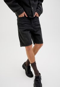 Zwarte denim shorts met een rechte snit, met een klassiek vijf-pocket ontwerp. Gecombineerd met zwarte schoenen en bruine gestructureerde sokken.