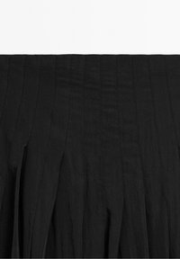 Jupe plissée noire avec des détails de couture verticale et plusieurs larges plis espacés de façon régulière.