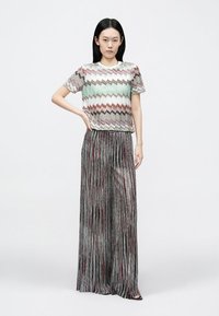 Mitmevärvilise ziganjoonelise mustriga lühikeste varrukatega kootud top, mida on kombineeritud volditud laia säärega metallist hõbedaste pükstega, millel on punased ja mustad aktsendid.