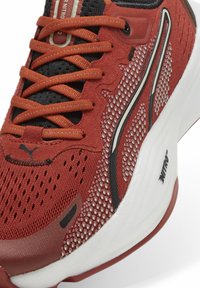 Baskets de sport rouges avec tissu en maille, accents noirs contrastants et lacets proéminents. Dotées d'une semelle blanche rembourrée et de détails de logo subtils.