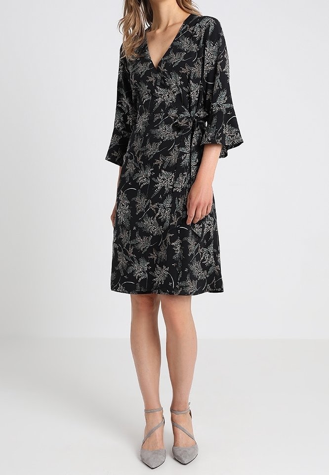 Vestido negro envolvente con escote en V y mangas acampanadas, que presenta un estampado floral en blanco y verde. Tejido suave y diseño hasta la rodilla.