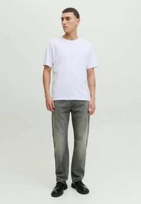 Λευκό βαμβακερό μπλουζάκι, κοντά μανίκια, συνδυασμένο με ανοιχτό γκρι τζιν παντελόνι με ξεθωριασμένο αποτέλεσμα, ολοκληρωμένο με μαύρα δερμάτινα παπούτσια.