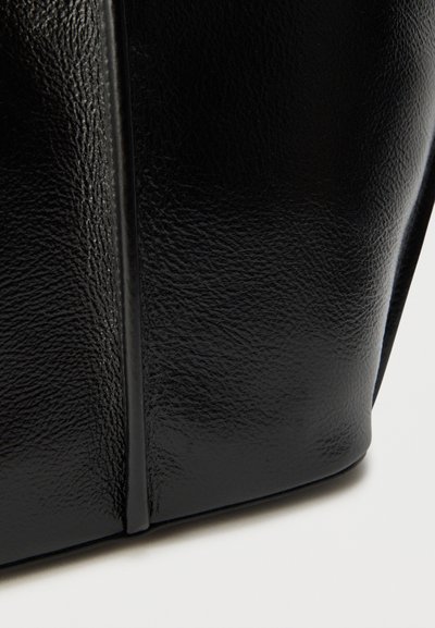 Μαύρη τσάντα χειρός από δέρμα με υφή και λείο φινίρισμα, που διαθέτει ελαφριά γυαλάδα και στιβαρό σχήμα, τονίζοντας καθαρές γραμμές και μινιμαλιστικό σχεδιασμό.