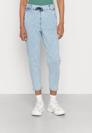 Pantalones jogger de denim azul claro con cintura ajustable, puños en los extremos y bolsillos laterales, combinados con zapatillas blancas y calcetines tobilleros.