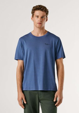 Maglietta a righe blu, maniche corte, collo rotondo, realizzata in cotone, con un piccolo logo nero sul petto a sinistra, abbinata a pantaloni verdi.