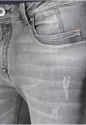 Gray denim jeans featuring a slim fit, subtle whiskering, and distressed details on the thigh. Includes a coin pocket and metal button closure.