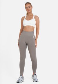Mallas de tiro alto gris claro con un diseño texturizado, combinadas con un sujetador deportivo blanco. Modelo lleva zapatillas plateadas y negras.