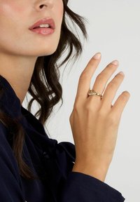 Anello d'oro con gemme trasparenti, caratterizzato da una fascia liscia e pietre aggiuntive sui lati, presentato su una mano con unghie dritte e curate.