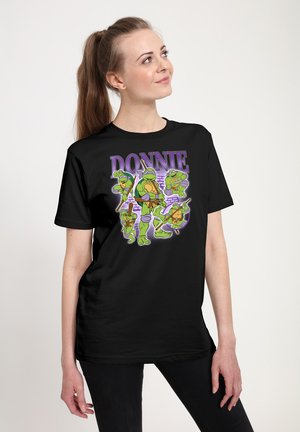 Femme portant un t-shirt noir avec cinq Tortues Ninja vertes et le texte "DONNIE" en violet au-dessus.