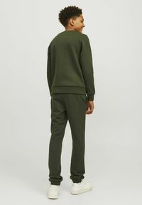 Mørkegrøn sweatshirt og matchende joggers lavet af blødt stof, med en afslappet pasform og ribbede manchetter, parret med hvide sneakers.