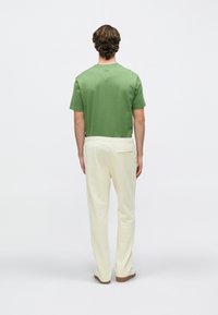 Πράσινο πουκάμισο με κοντά μανίκια και ελεφαντόδοντου παντελόνια με άνετη εφαρμογή. Τα παντελόνια διαθέτουν ελαστική μέση και λεπτομέρεια πίσω τσέπης.