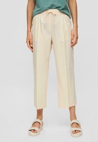 Pantalons cropped beige clair, avec une taille élastique et un cordon de serrage. Texture lisse, design minimal, associés à des sandales tressées.