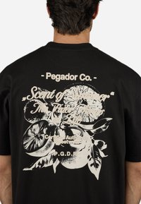Sort bomulds t-shirt med et hvidt blomster grafisk design med citrusmotiver og tekst, placeret på ryggen. Casual pasform, korte ærmer.