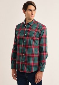 Camisa de cuadros verde y rojo, con botones, de manga larga y cuello clásico; presenta botones blancos y una textura de tela suave.