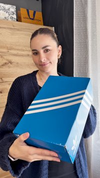 Plava kutija za Adidas cipele s tri bijele dijagonalne pruge i logotipom marke. Kutija izgleda sjajno, s pažljivo presavijenim kutovima.