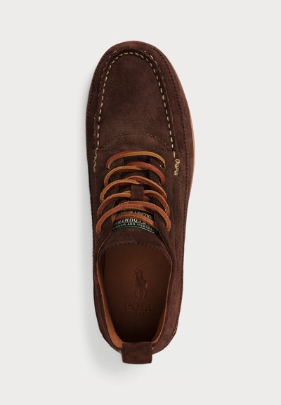 Brown suede moccasin shoe with tan laces and stitching. Features a branded insole with a logo and a rounded toe design.