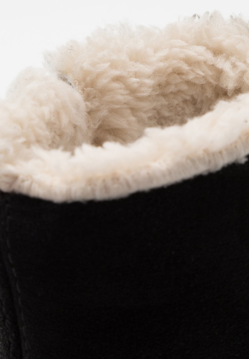 Schwarze Wildlederstiefel mit einem weichen, cremefarbenen Kunstfellfutter am Schaft, das die plüschige Textur und die kontrastierenden Farben hervorhebt.