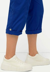 Baskets blanches avec une semelle épaisse, finition texturée et design à lacets. Pantalons courts bleus avec poignets retroussés et détails en bouton argent.
